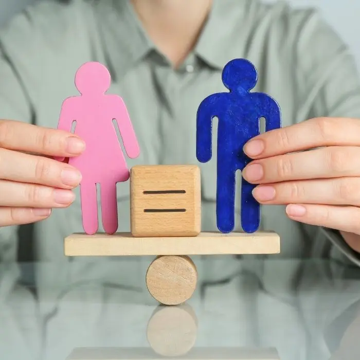 Persona sujetando muñecos de diferente género en balanza para representar igualdad